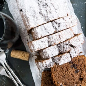Top-down shot of a loaf of red wine cake cut into slices. There's a glass of red wine, a cork and some forks next to it.