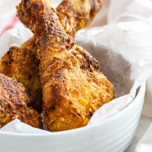 breaded chicken drumsticks in a white bowl with parchment paper