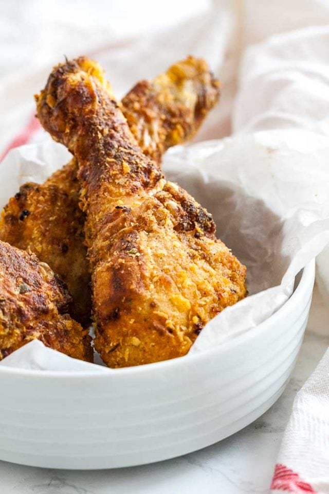 breaded chicken drumsticks in a white bowl with parchment paper