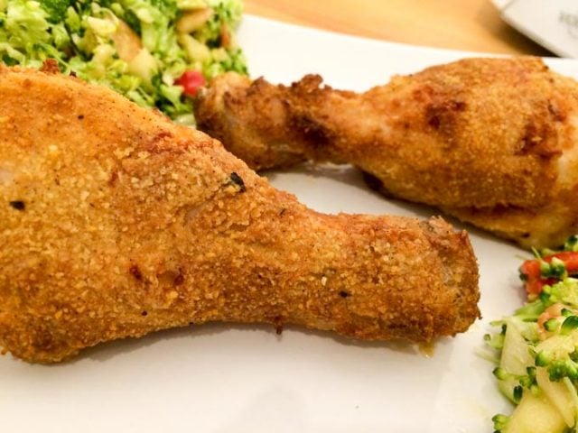 two breaded chicken drumsticks pm a parchment paper with zucchini salad in the background