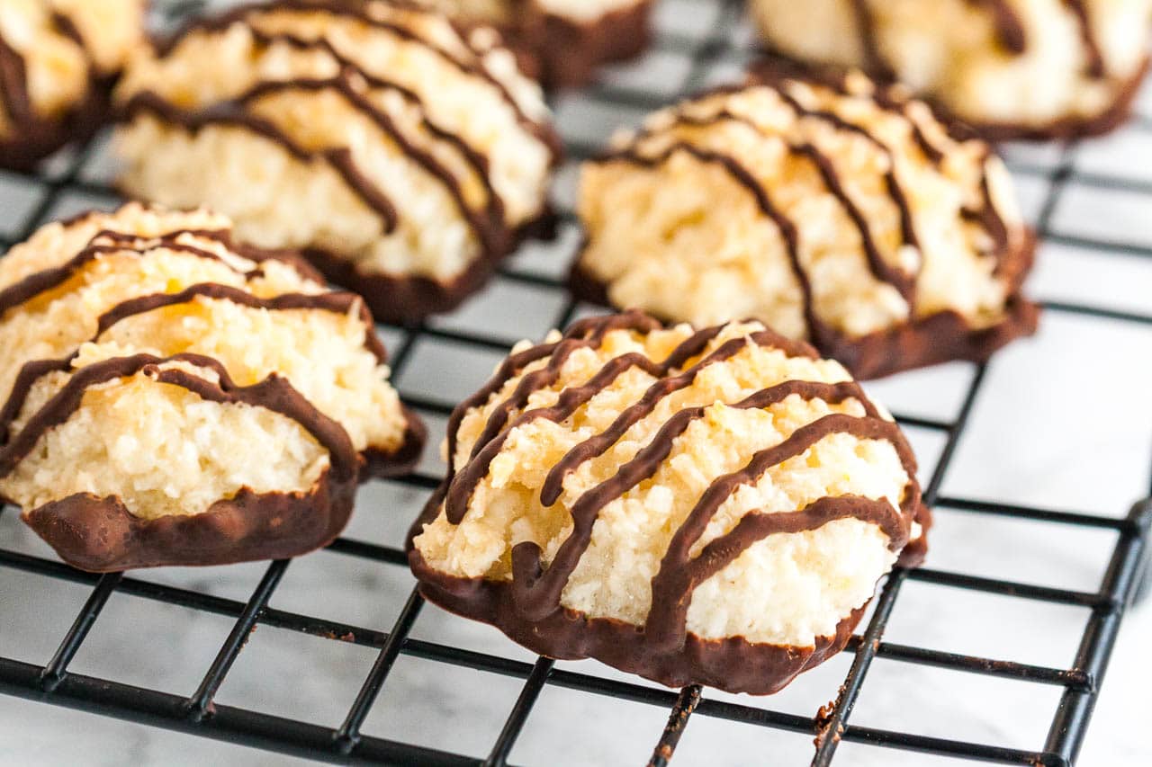 Coconut macaroons with chocolate bottoms and stripes on a black cooling rack.