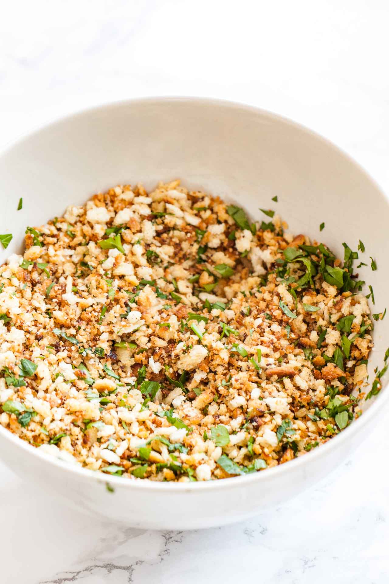 A white bowl with breadcrumbs and parsley mixture.