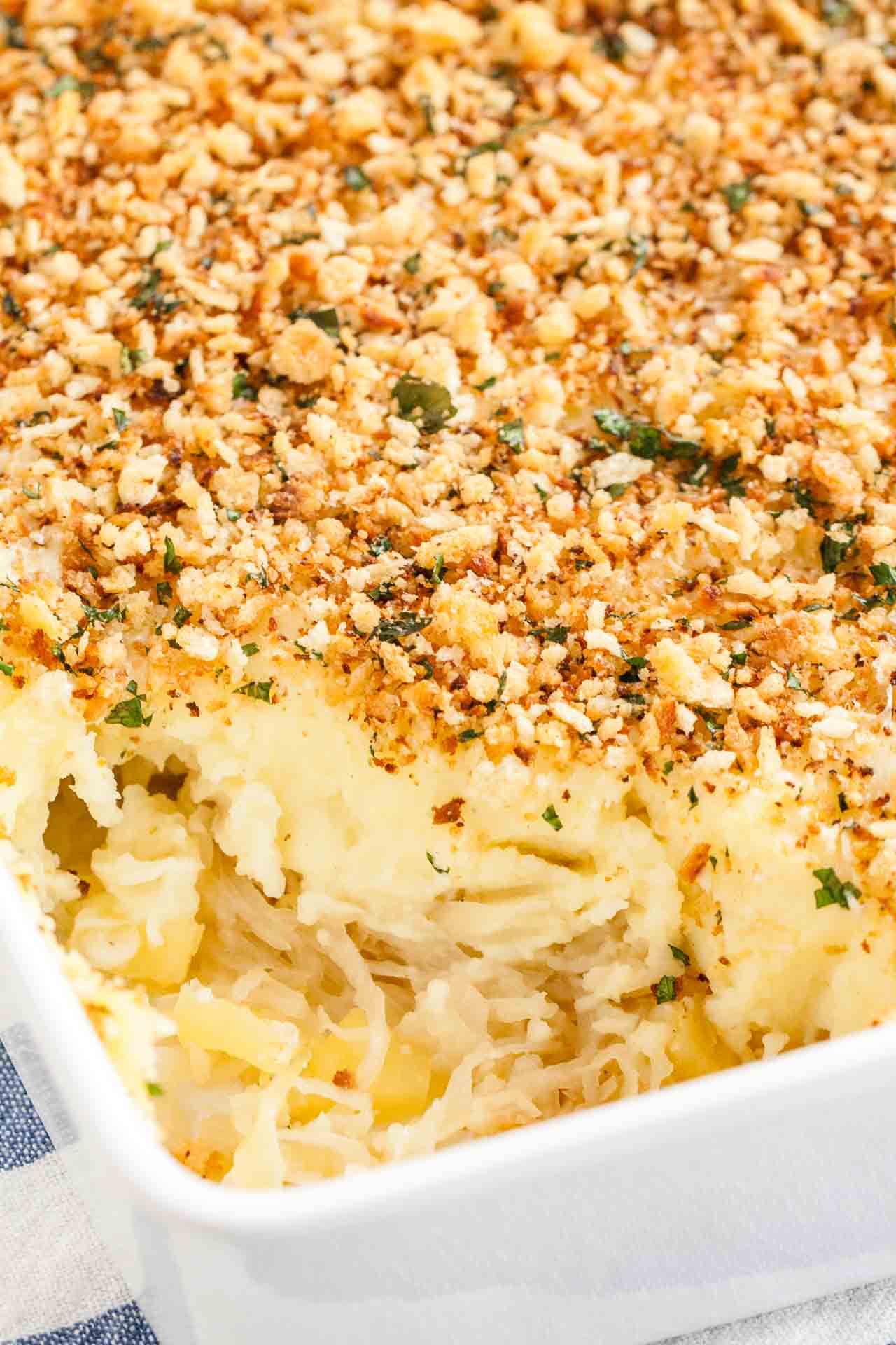 Close-up of a white baking dish with sauerkraut mashed potato casserole on a white and blue dishtowel. A portion of the casserole has been removed.