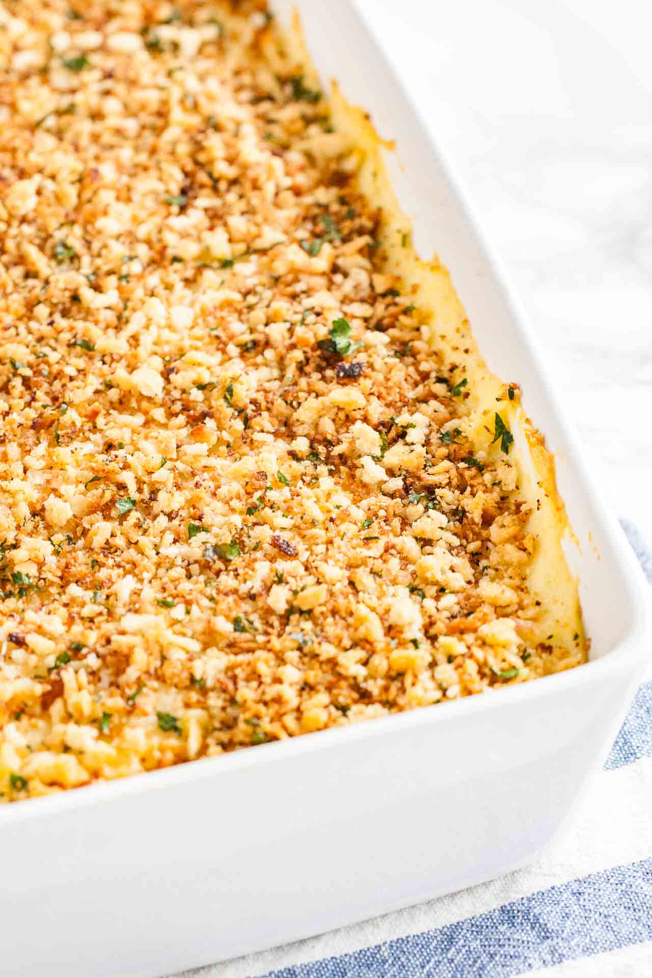 Close-up of a white baking dish with sauerkraut mashed potato casserole on a white and blue dishtowel.