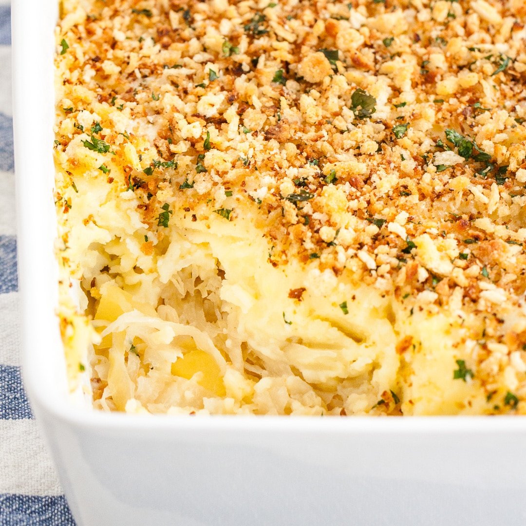 Close-up of a white baking dish with sauerkraut mashed potato casserole on a white and blue dishtowel. A portion of the casserole has been removed.