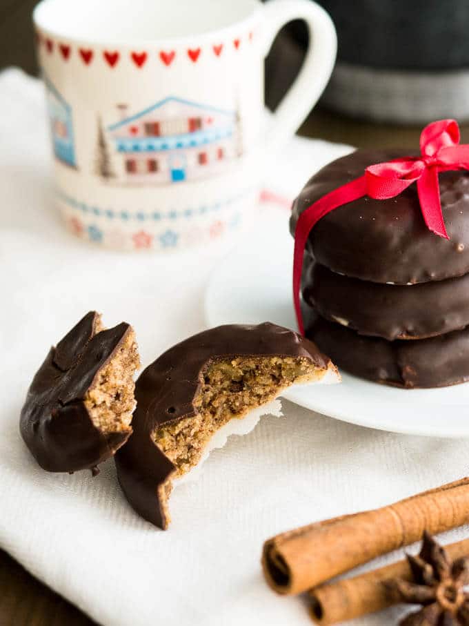 A stack of Lebkuchen on a white plate tied together by a red bow. Next to it a coffee mug and a Lebkuchen broken in two pieces.