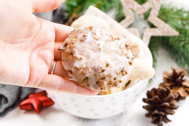 A hand holding a lebkuchen glazed with sugar. There is a white bowl with Christmas cookies in the background