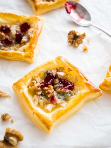 Pear and gorgonzola mini tartlets with cranberry sauce on white parchment paper garnished with walnuts and with a spoon next to it.