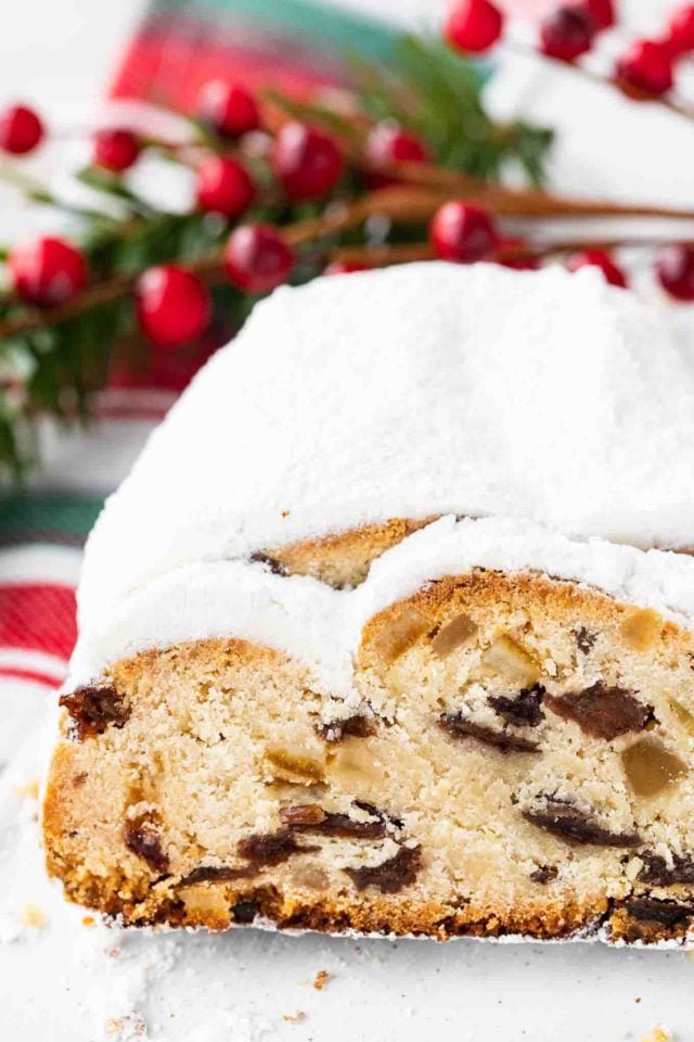 half a christstollen with a slice cut off on a red, white and green dish towel with cranberries in the background.