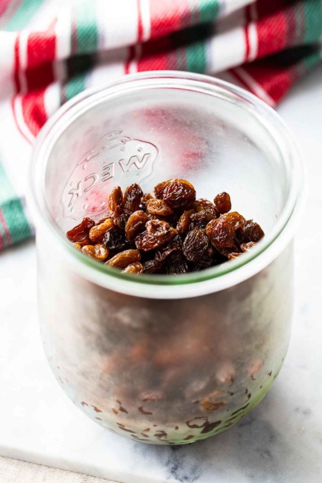 A weck jar with raisins next to a red white and green dish towel.