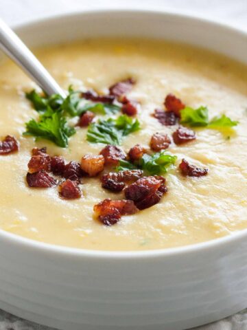 Close-up of a white bowl of potato soup topped with bacon and parsley with a spoon in it.