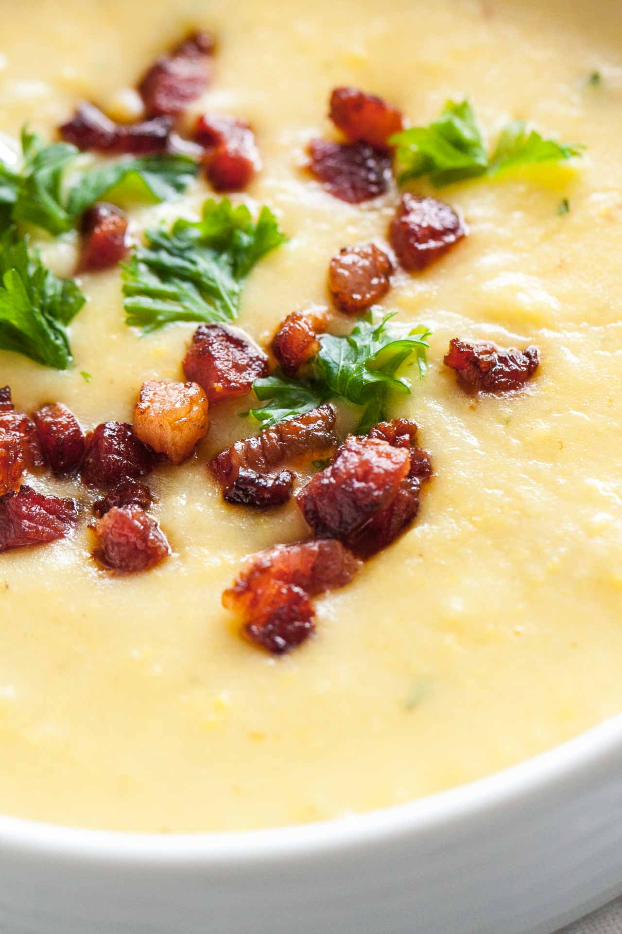 Close-up of a white bowl of potato soup topped with bacon and parsley with a spoon in it.
