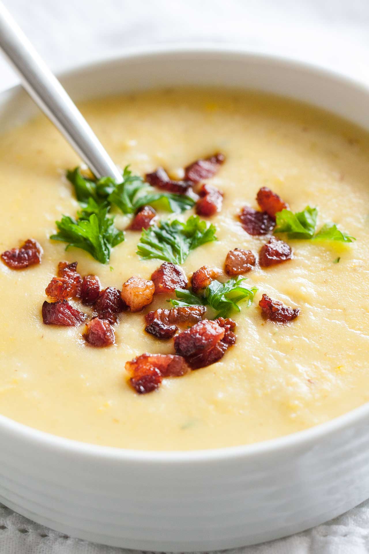 Close-up of a white bowl of potato soup topped with bacon and parsley with a spoon in it.