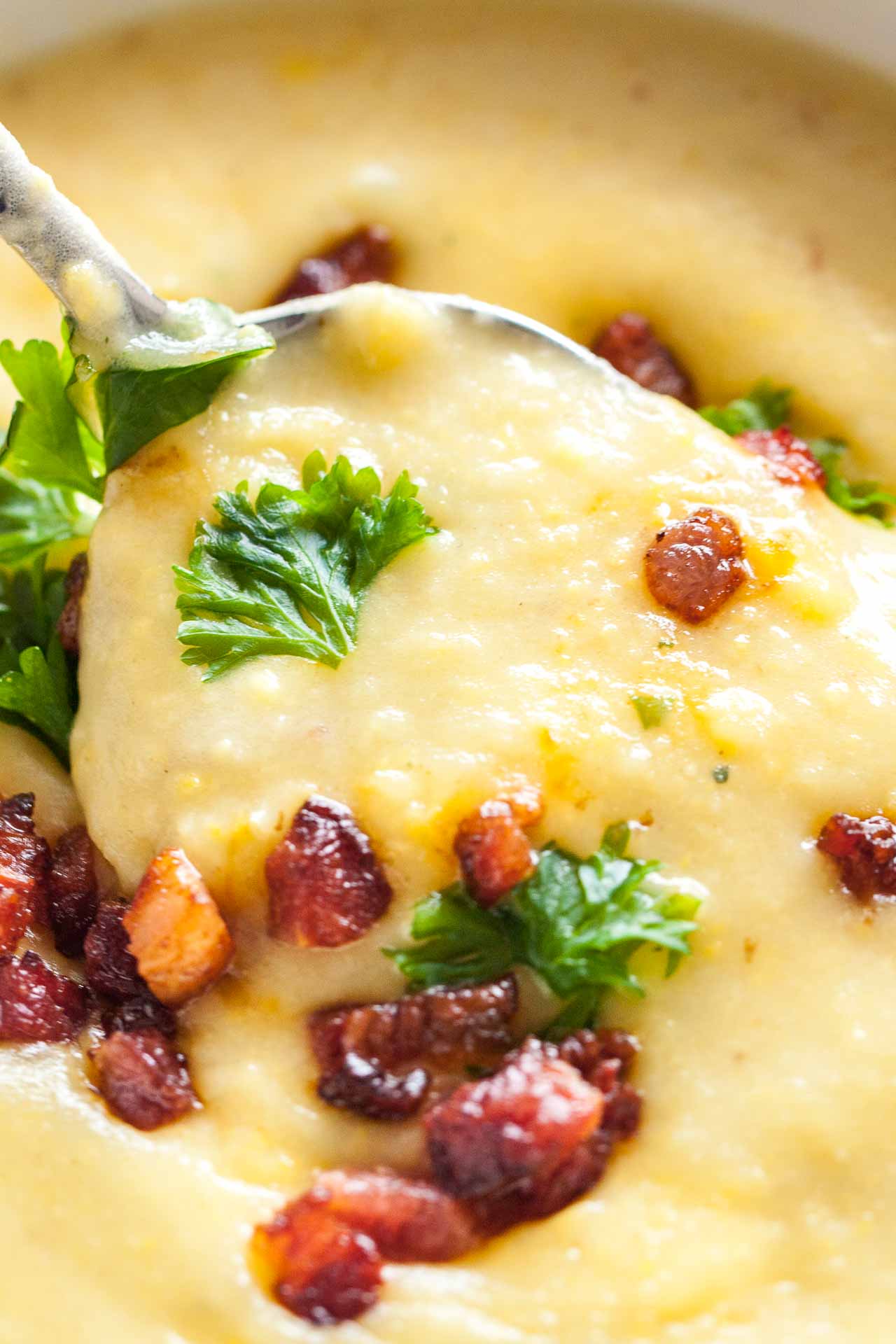 Close-up of a spoon lifting up a portion of potato soup topped with bacon and parsley.