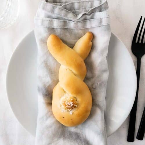 A bunny-shaped bread roll on a napkin set on a plate.