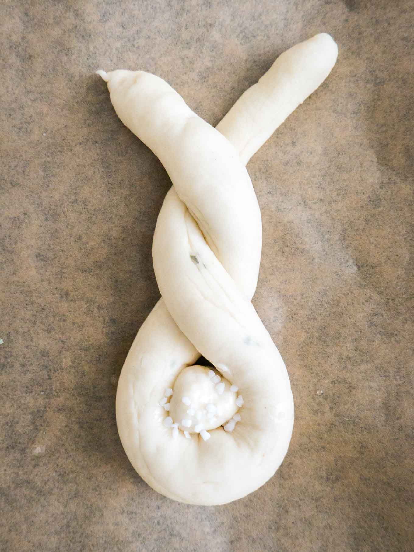 Dough shaped like a bunny, with a cottontail from dough on brown parchment paper.