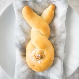 Bread shaped like a bunny, with a cottontail from dough on a grey dishtowel on a white plate.