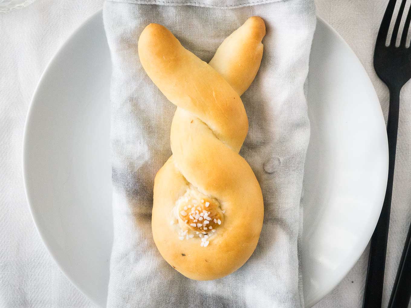 Bread shaped like a bunny, with a cottontail from dough on a grey dishtowel on a white plate.