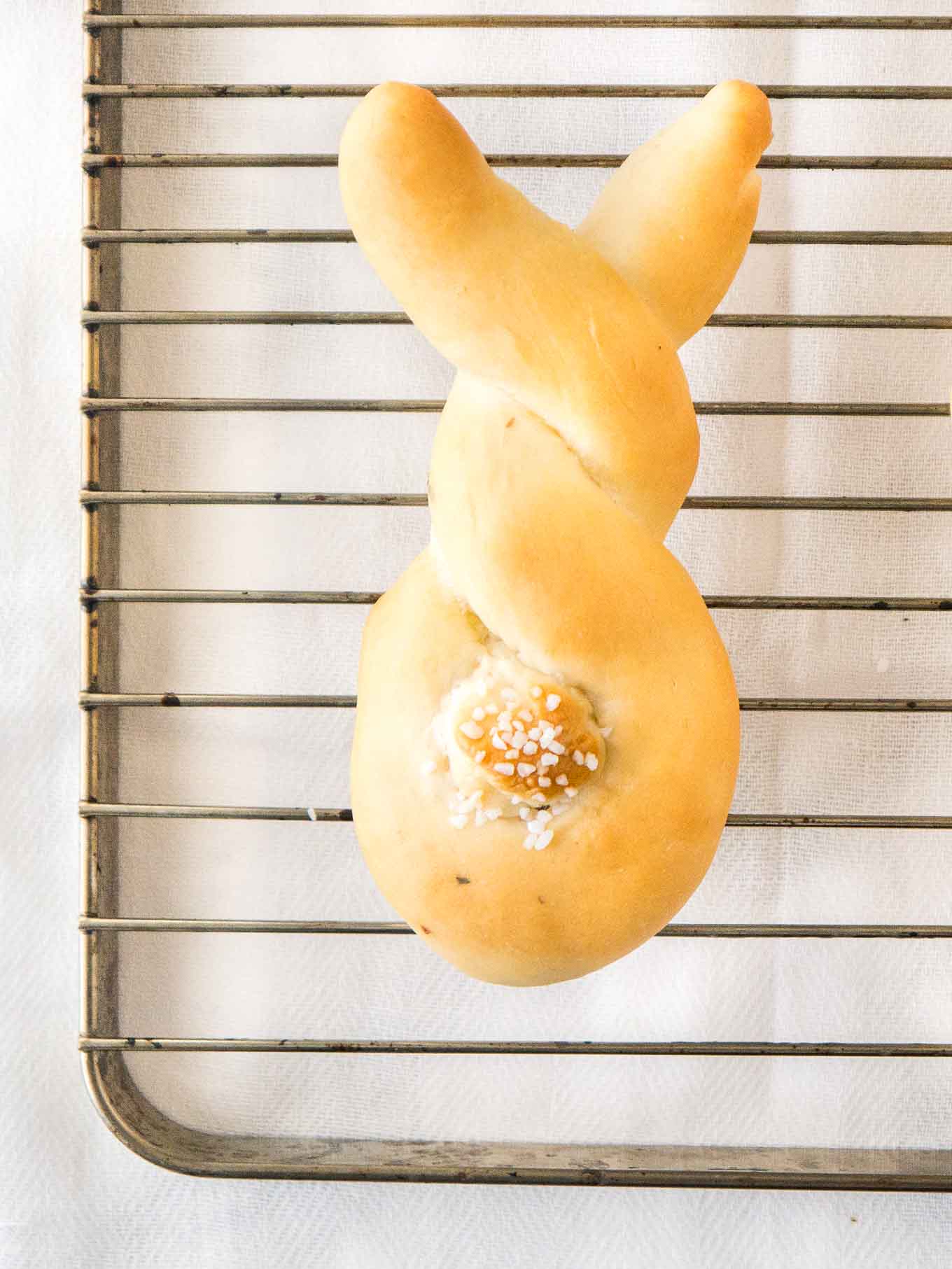 Bread shaped like a bunny, with a cottontail from dough on a stainless steel cooling rack.