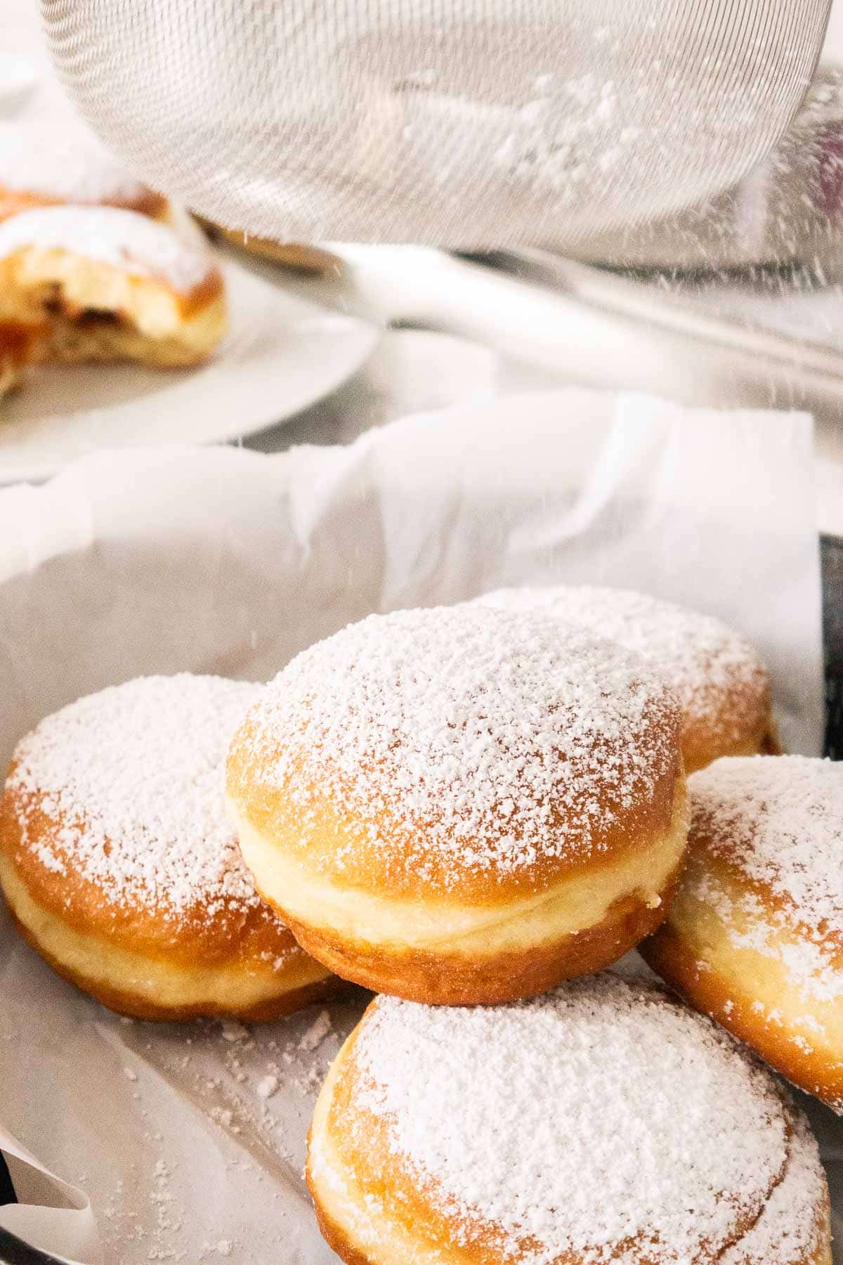 Krapfen getting dusted with powdered sugar.
