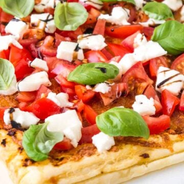 Close-up of tomato mozzarella puff pastry pizza with tomatoes, mozzarella, basil leaves and balsamic glaze.
