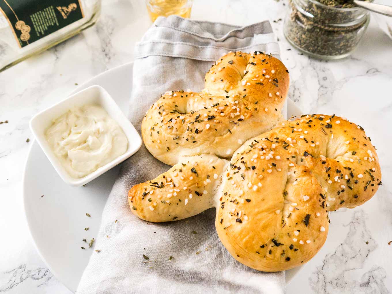 Bread shaped like a shamrock on a grey dishtowel next to a small square bowl of dipping sauce on a plate.