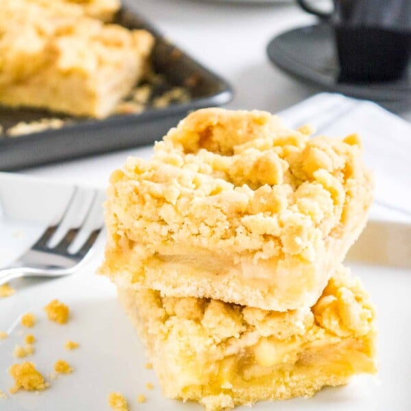 two pieces of apple streusel cake stacked on top of each other on parchment paper with a fork next to it and a baking sheet in the background
