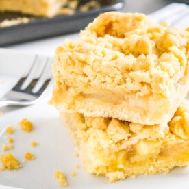 two pieces of apple streusel cake stacked on top of each other on parchment paper with a fork next to it and a baking sheet in the background