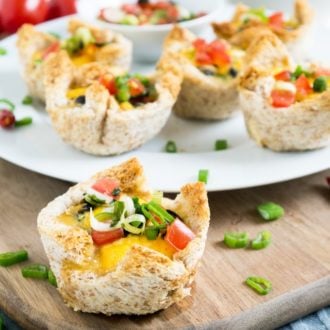 A white plate with cheesy Mexican toast cups garnished with chives on a wooden cutting board. There's a single toast cup in front.