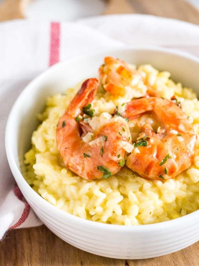 Close-up of a white bowl with saffron risotto with fried shrimp on a white dish towel with a red stripe.