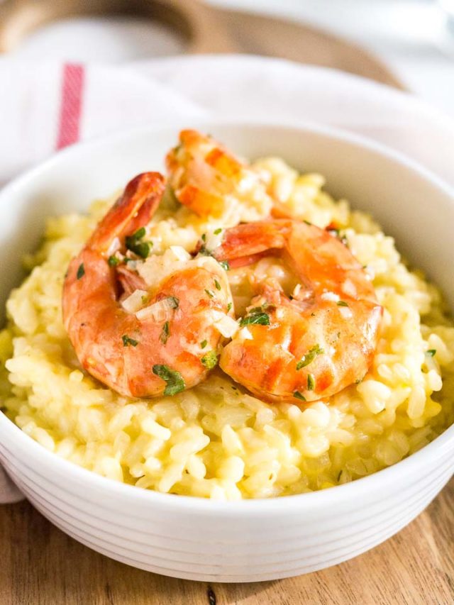 Close-up of a white bowl with saffron risotto with fried shrimp on a white dish towel with a red stripe.