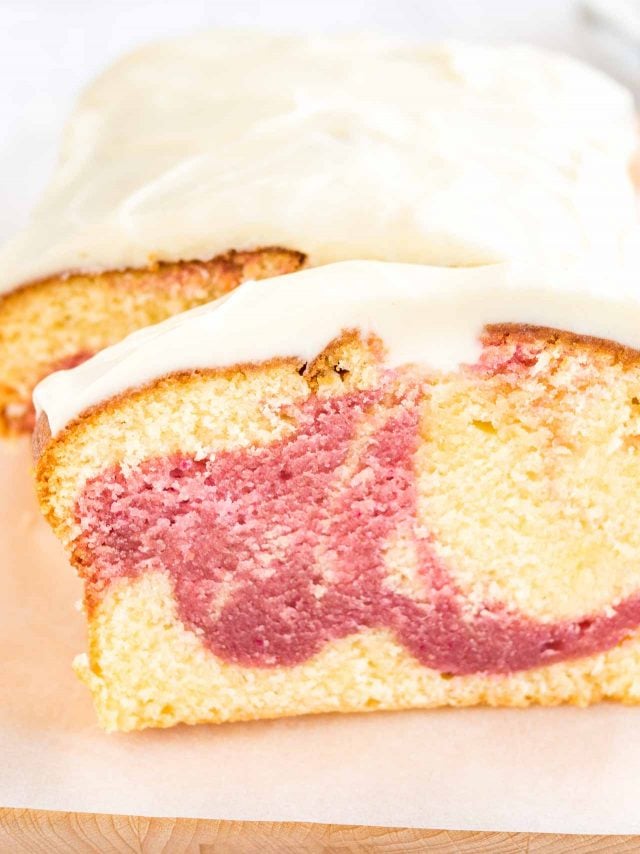Close-up of a loaf of raspberry swirl pound cake sitting on a wooden cutting board lined with parchment paper. A slice has been cut off and is leaning against it.