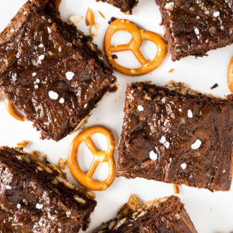 Top-down shot of salted caramel pretzel brownies with nutella on white parchment with some pretzels.