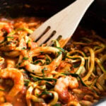 A pan of linguine with calamary and prawn tomato sauce with a slotted spatula in it.