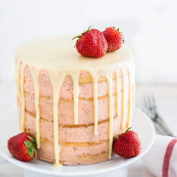 A white plate with naked strawberry layer cake garnished with strawberries next to a white dishtowel with a red stripe and some forks.