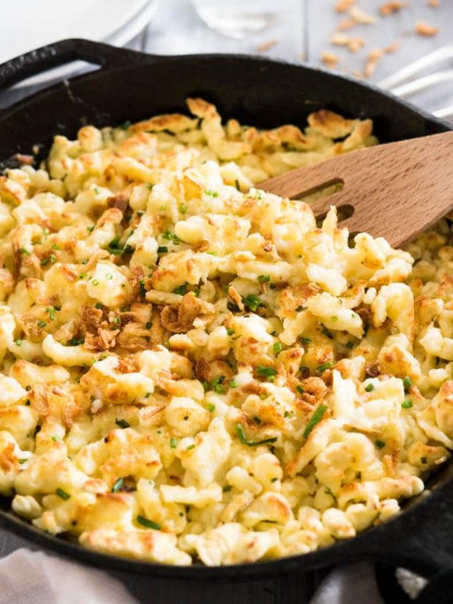 A cast-iron pan with cheese spaetzle. A slotted spatula is digging into it.
