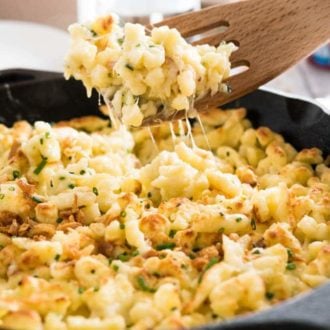 A cast-iron pan with cheese spaetzle. A slotted spatula is lifting out a portion.