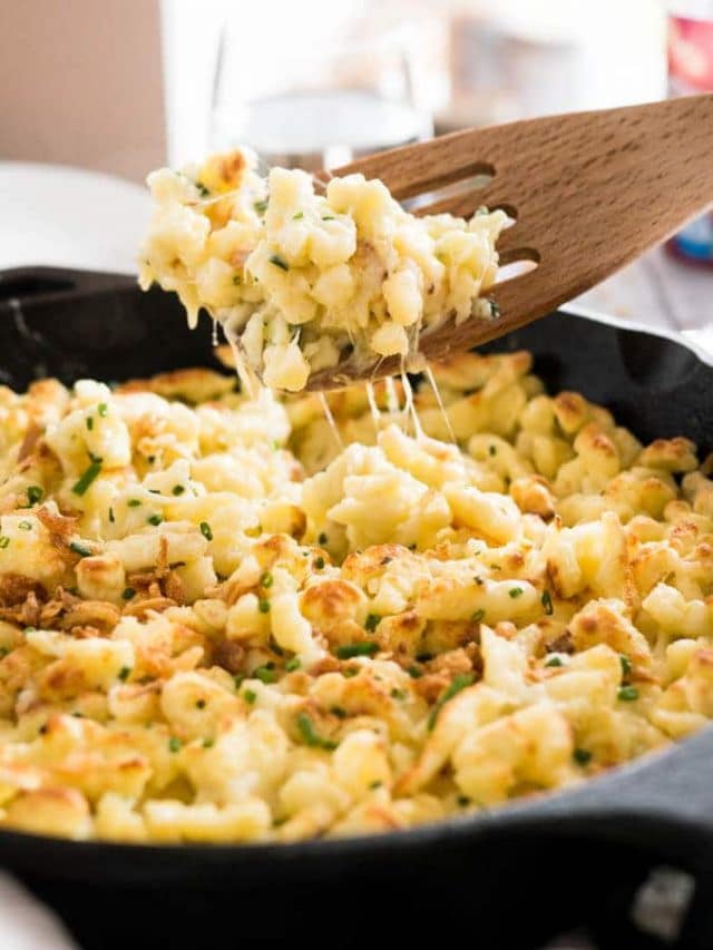 A cast-iron pan with cheese spaetzle. A slotted spatula is lifting out a portion.