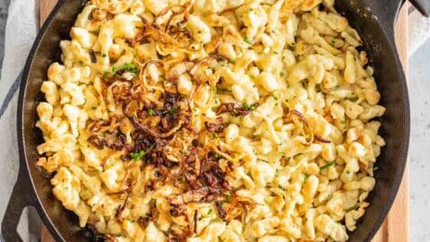 Käsespätzle in a cast iron pan on a wooden board.