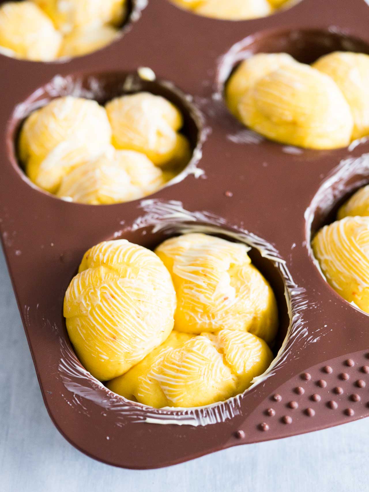 A buttered muffin pan with 3 pieces of dough in each hole. Each piece has butter on top.