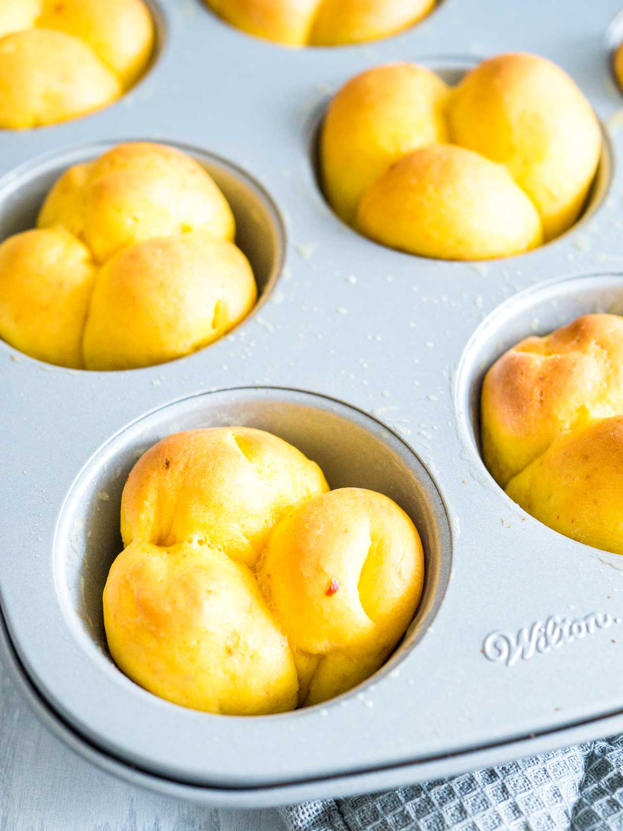 A muffin pan with baked pumpkin dinner rolls in it.