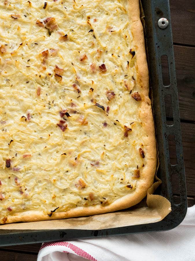 Top-down shot of a baking sheet lined with parchment paper with onion tart on a wooden table.