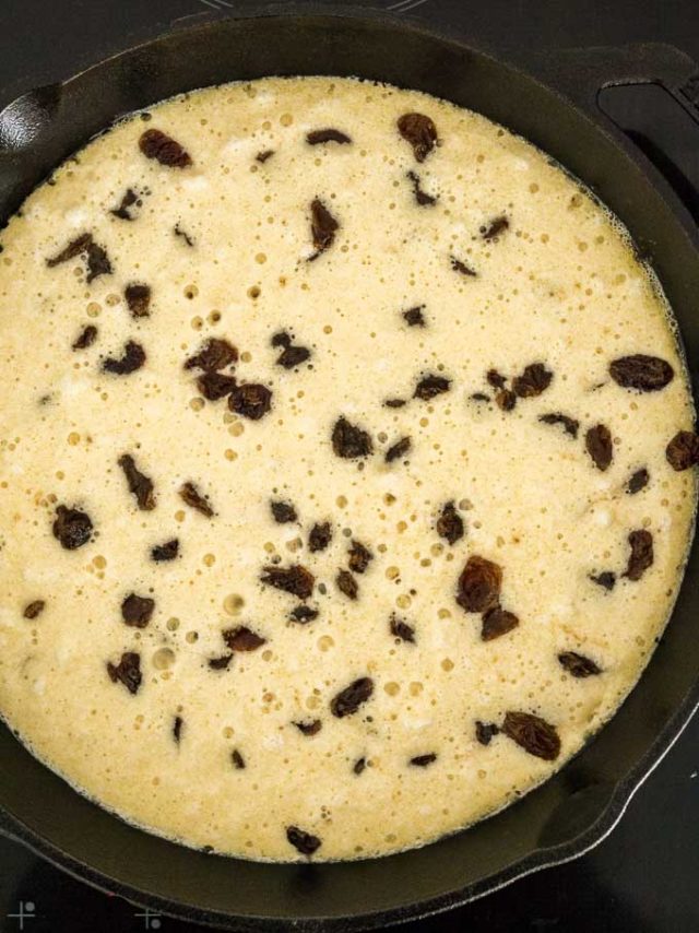 Pancake batter with raisins in a lodge pan.