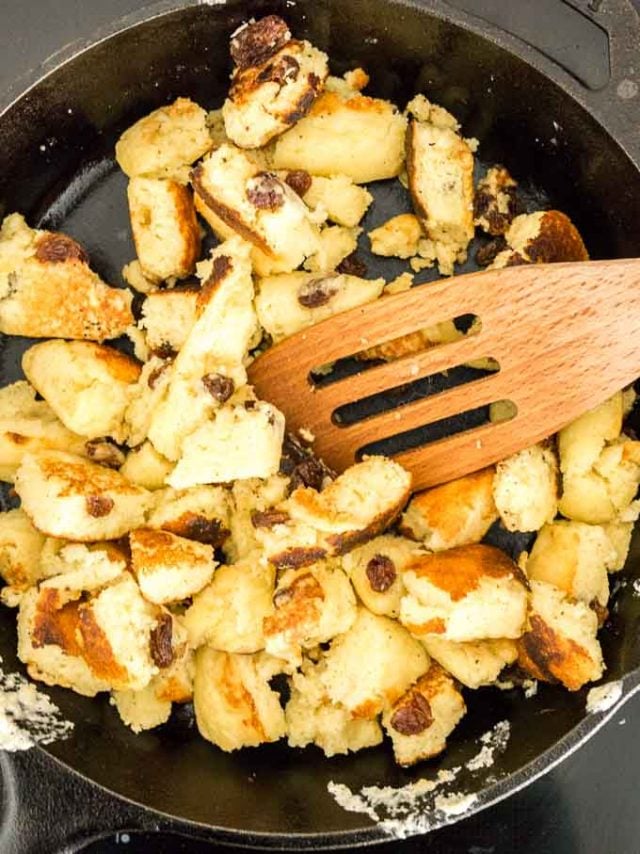 Torn, cooked pancakes with raisins in a lodge pan with a slotted wooden cooking spatula.