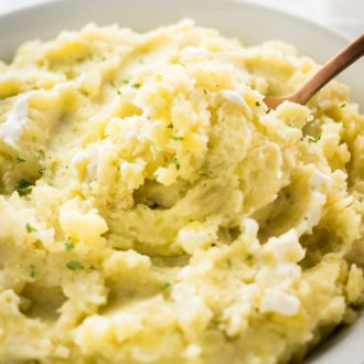 A white bowl with mashed potatoes garnished with parsley with a bronze spoon in it.