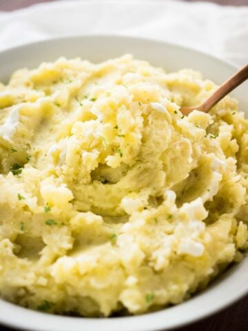 A white bowl with mashed potatoes garnished with parsley with a bronze spoon in it.