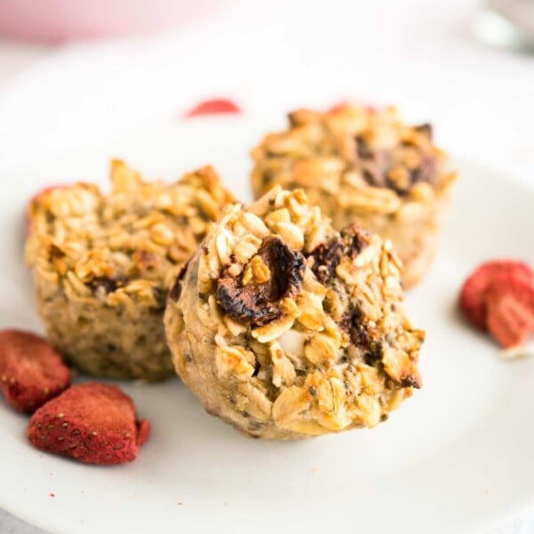 Three strawberry baked oatmeal cups on a white plate garnished with some dried strawberries.