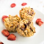 Three strawberry baked oatmeal cups on a white plate garnished with some dried strawberries.