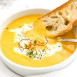 A bowl of carrot soup with sour cream and chili threads with a toasted slice of bread and a spoon in it.