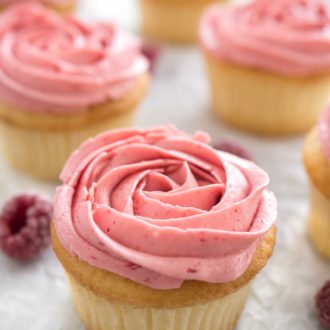 Raspberry lemon cupcakes with pink raspberry frosting next to some raspberries.